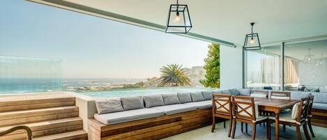 A modern outdoor seating area with a view of the ocean, wooden steps, and a dining table with chairs.