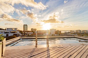 Ein Dachpool mit Blick auf die Stadtlandschaft, darunter moderne Gebäude und ein Sonnenuntergang.