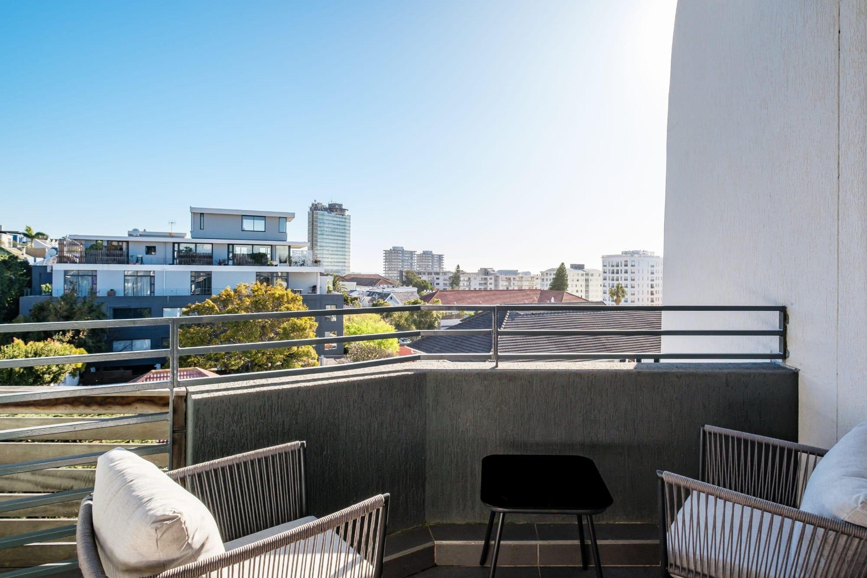 Un balcon agrémenté de fauteuils en osier et d’une petite table, offrant une vue sur un paysage urbain dominé par des bâtiments modernes.