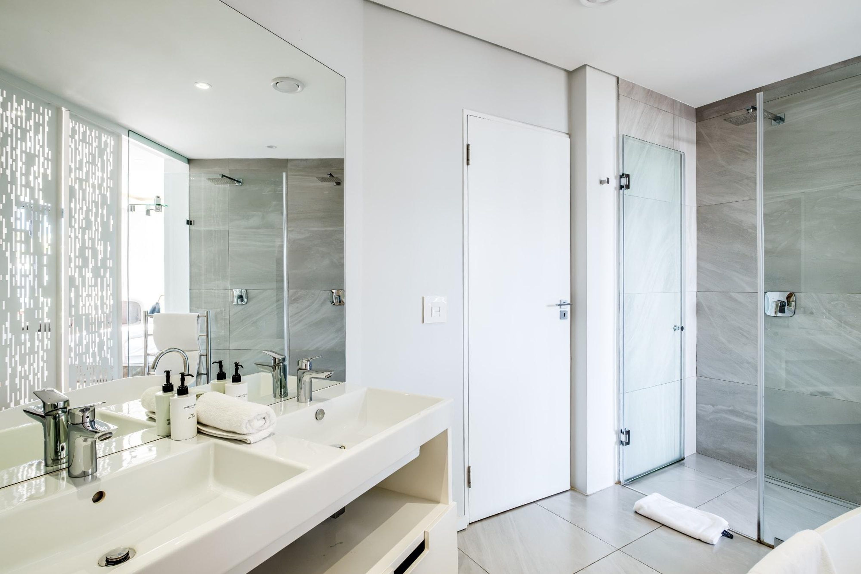 Ein modernes Badezimmer mit einem großen Spiegel, zwei Waschbecken, einer Dusche und einer gläsernen Duschkabine.