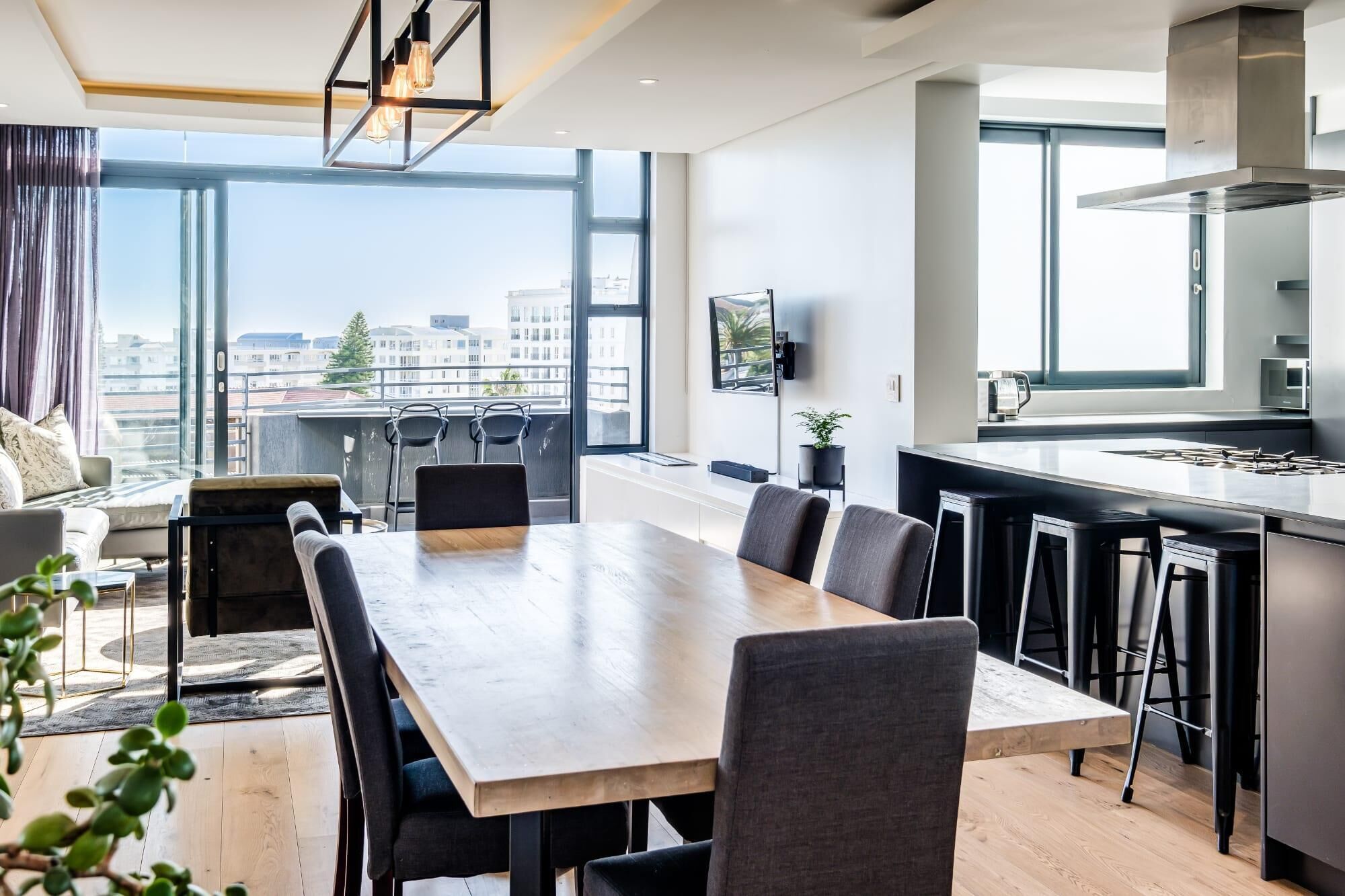 A modern kitchen with a large island, a dining area with a long table, and a view of the city through large windows.