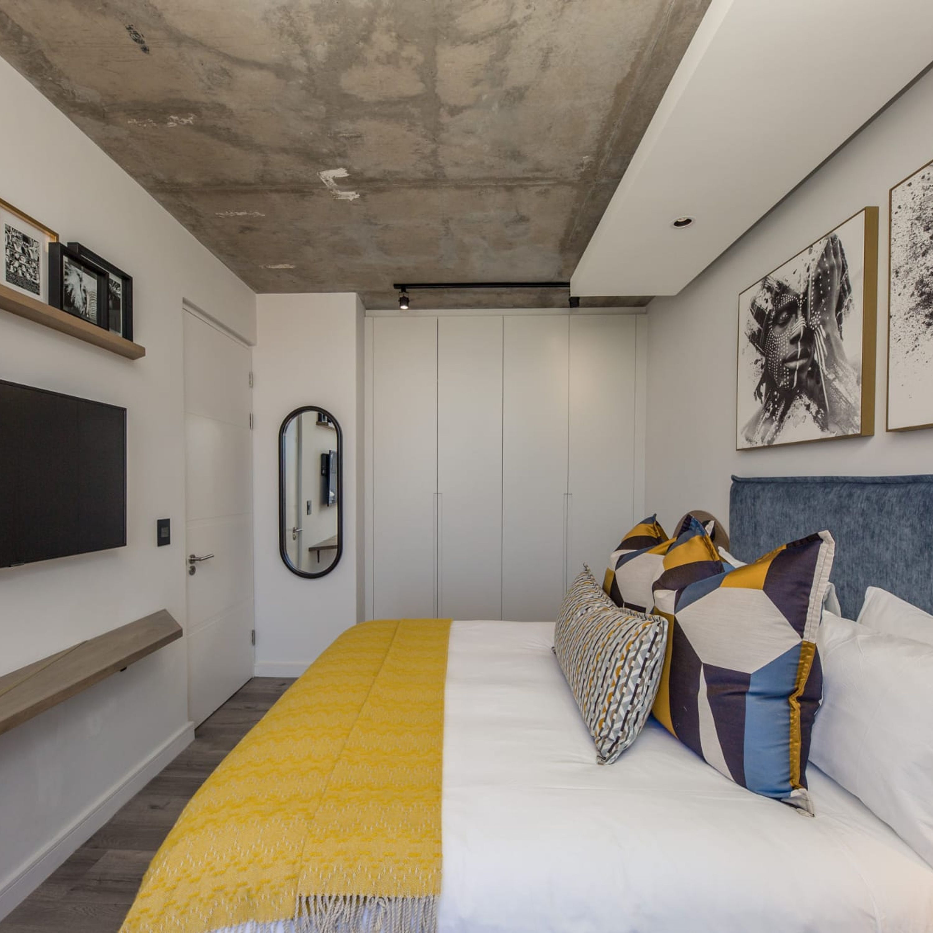 A modern bedroom with a bed, a mirror, a TV, and artwork on the walls.