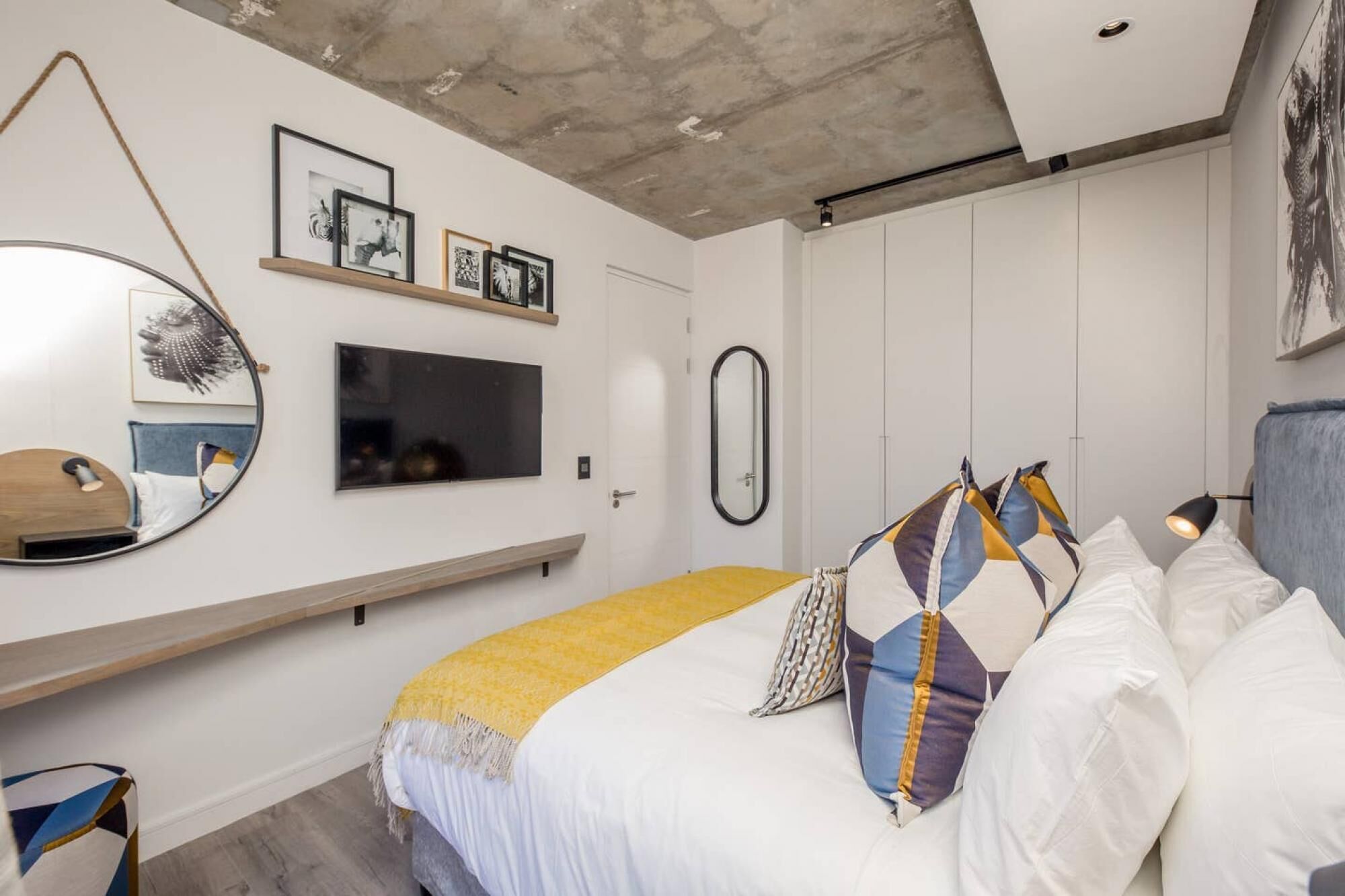 Un dormitorio con cama, televisor, espejo y repisa con fotografías.