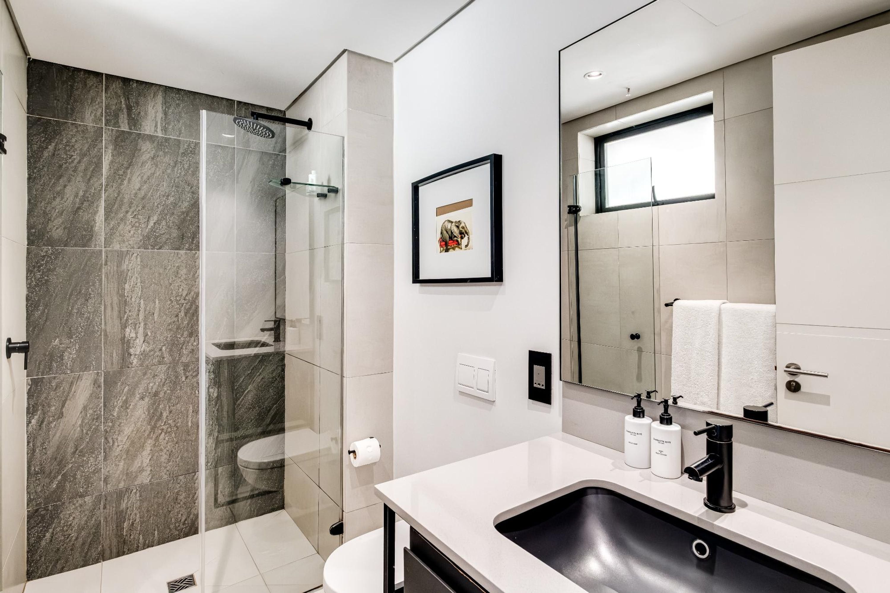 Un baño moderno con ducha de vidrio, un espejo grande y un lavabo blanco.