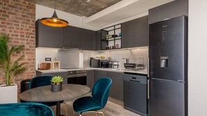 A modern kitchen with dark cabinetry, a black refrigerator, and teal chairs. - Beautifully Decorated Apartment in Cape Town Urban Signature (Cape Town)