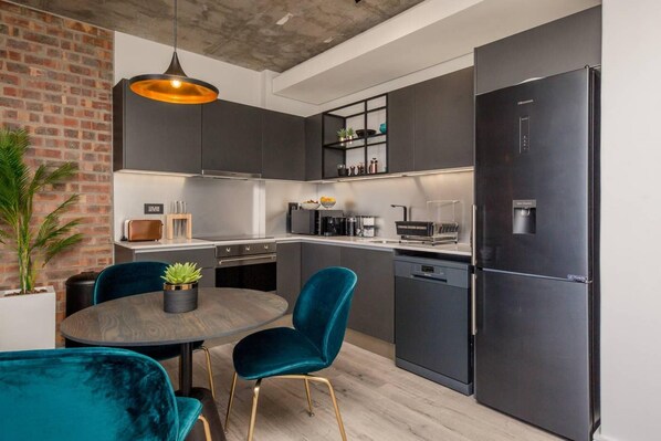 A modern kitchen with dark cabinetry, a black refrigerator, and teal chairs. - Beautifully Decorated Apartment in Cape Town Urban Signature (Cape Town)