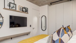 A modern bedroom with a bed, a TV, a mirror, and framed pictures on the wall. - Beautifully Decorated Apartment in Cape Town Urban Signature (Cape Town)