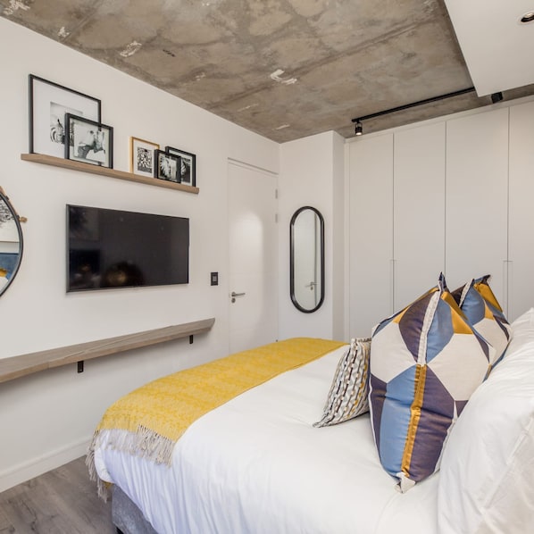 Una camera da letto moderna con un letto, una TV, uno specchio e quadri appesi al muro.