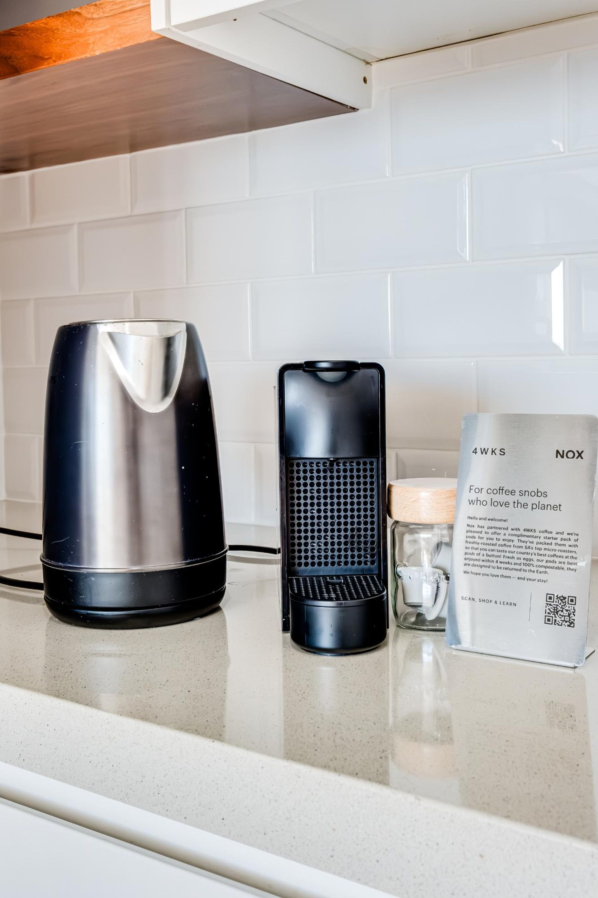 A kitchen counter with a coffee maker, a kettle, and a packet of coffee pods.