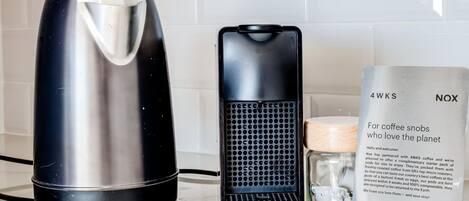 A kitchen counter with a coffee maker, a kettle, and a packet of coffee pods.