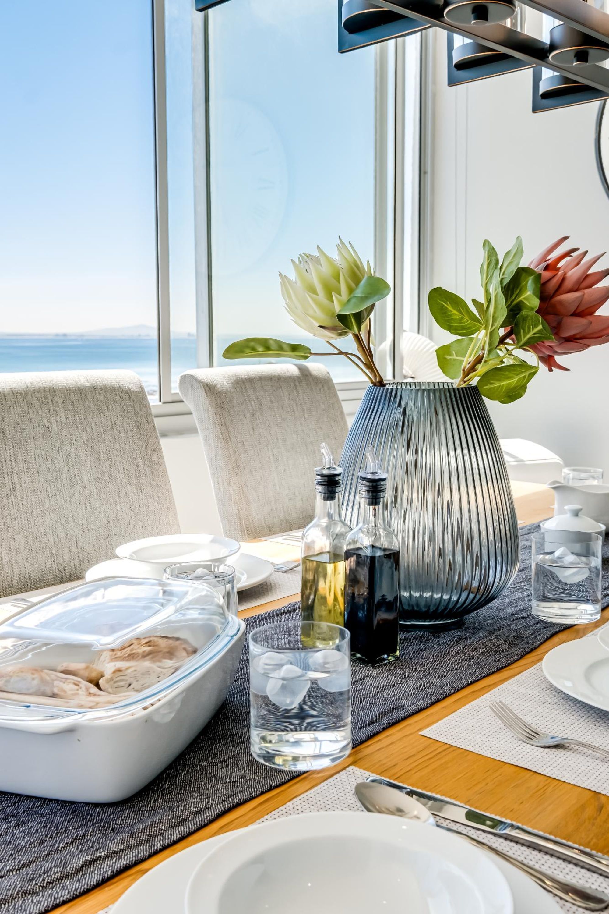 Ein Esstisch ist gedeckt mit Tellern, Besteck, einer Blumenvase und einem Glas Wasser.