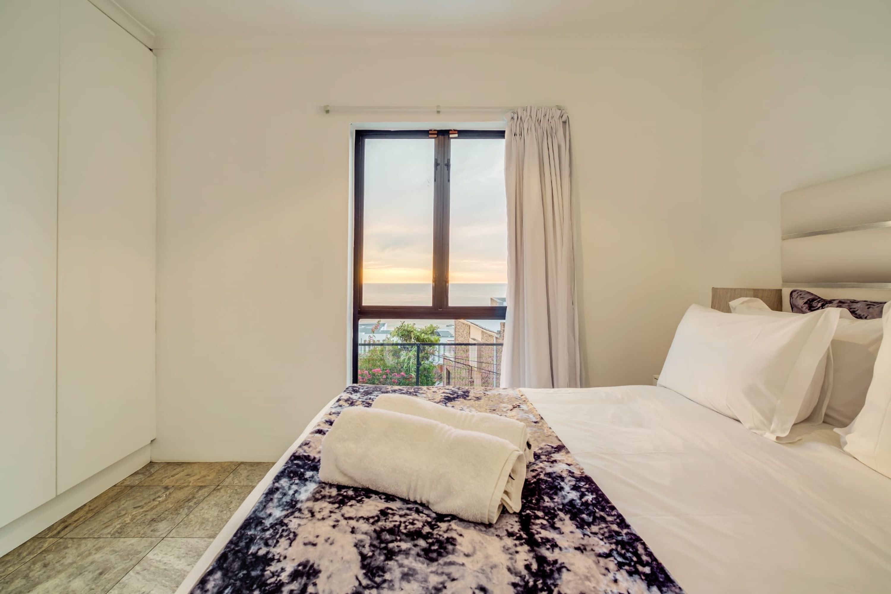 A hotel room with a bed, a window with curtains, and a view of the outside.