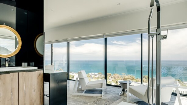 A modern bathroom with a large bathtub, a white chair, and a view of the ocean. - Camps Bay Holiday Villa With Sunset Views Sunset Views (Cape Town)