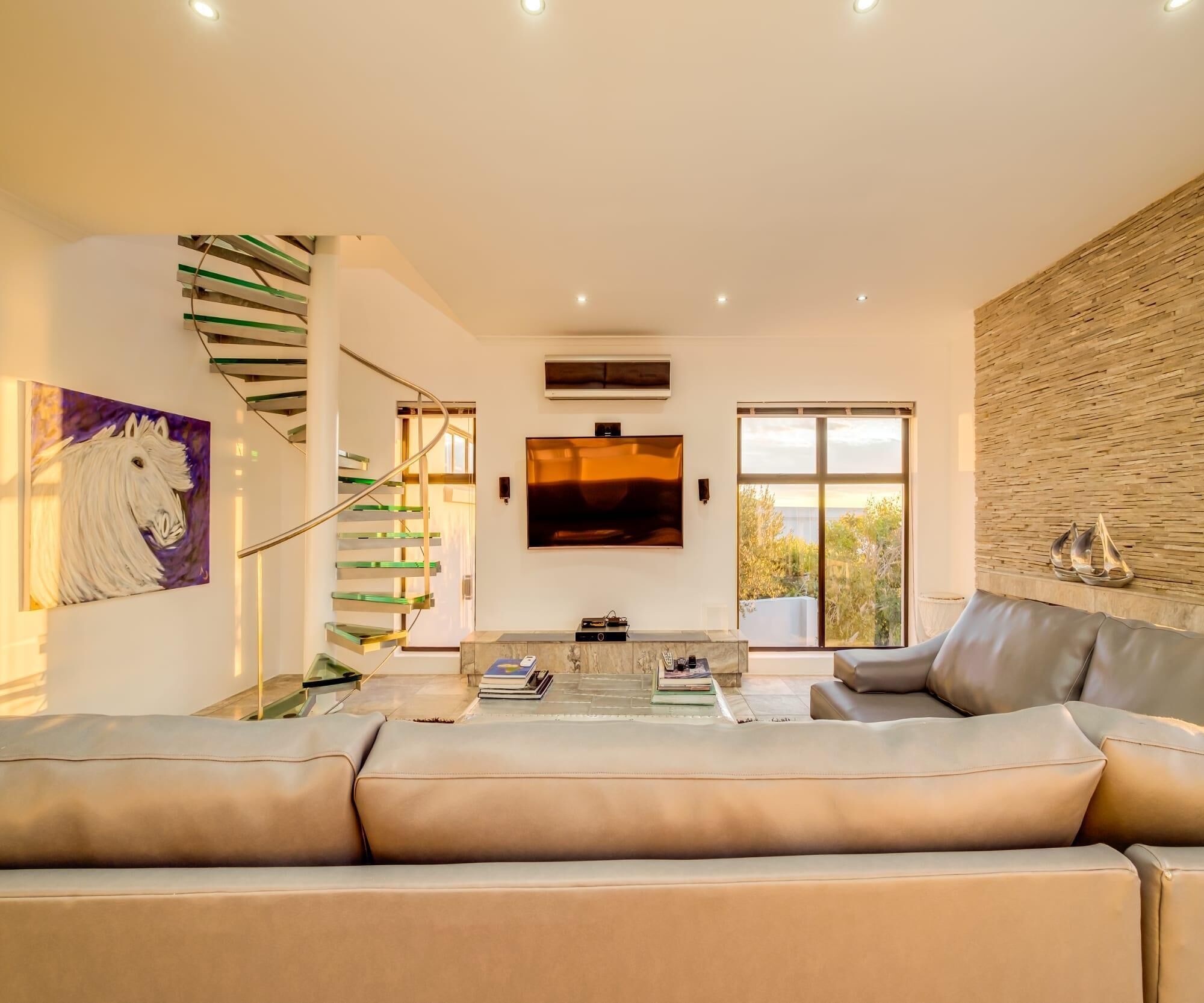 Ein modernes Wohnzimmer mit einer großen Couch, einem an der Wand montierten Fernseher und einer Treppe mit Glastrennläufen.