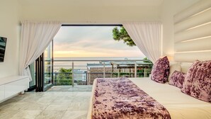 A bedroom with a bed, curtains, a TV, and a balcony with a view. - Camps Bay Holiday Villa With Sunset Views Sunset Views (Cape Town)