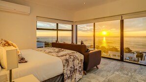 A bedroom with a bed, a sofa, and large windows offering a sunset view. - Camps Bay Holiday Villa With Sunset Views Sunset Views (Cape Town)