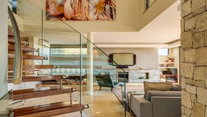 Um interior moderno com escada, sala de estar com sofá, lareira e televisão.