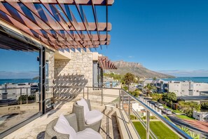 Ein Balkon mit Korbmöbeln, einer Steinmauer und Blick auf Meer und Berge.