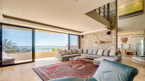 Uma sala de estar ampla, com um sofá grande, uma mesa de centro e vista para o oceano.