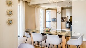 A modern kitchen with a glass dining table, four chairs, a chandelier, and a refrigerator. - Green Point Apartment Walking Distance to Stadium 407 Royal (Cape Town)