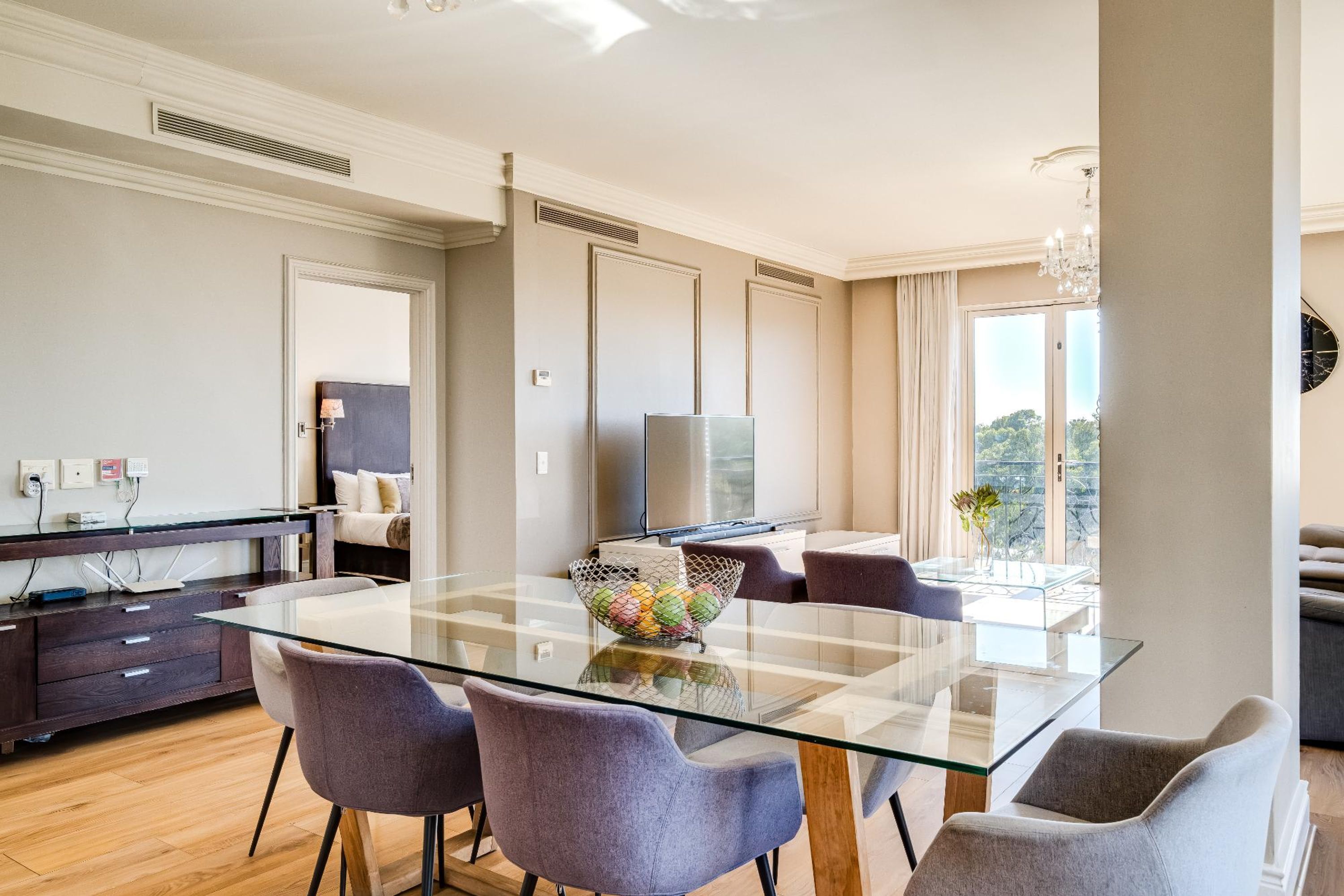 Un espace repas moderne avec une table en verre, des chaises grises, un panier décoratif et une vue sur l’extérieur.