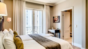 A hotel room with a large bed, a desk, a chair, a lamp, a painting, and a view of the outside. - Green Point Apartment Walking Distance to Stadium 407 Royal (Cape Town)