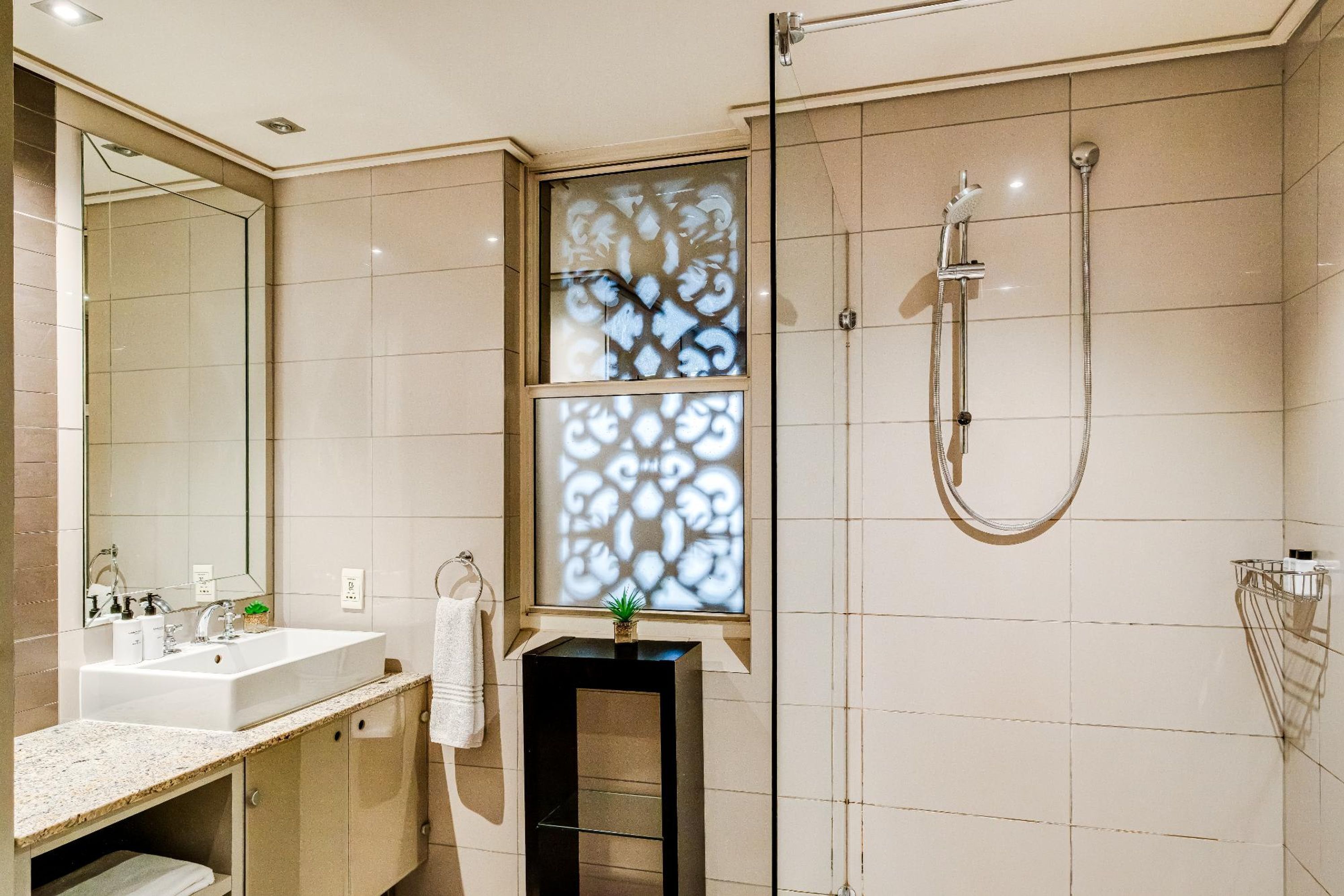 Un baño moderno con un espejo grande, un lavabo, ducha y un ventanal decorativo.