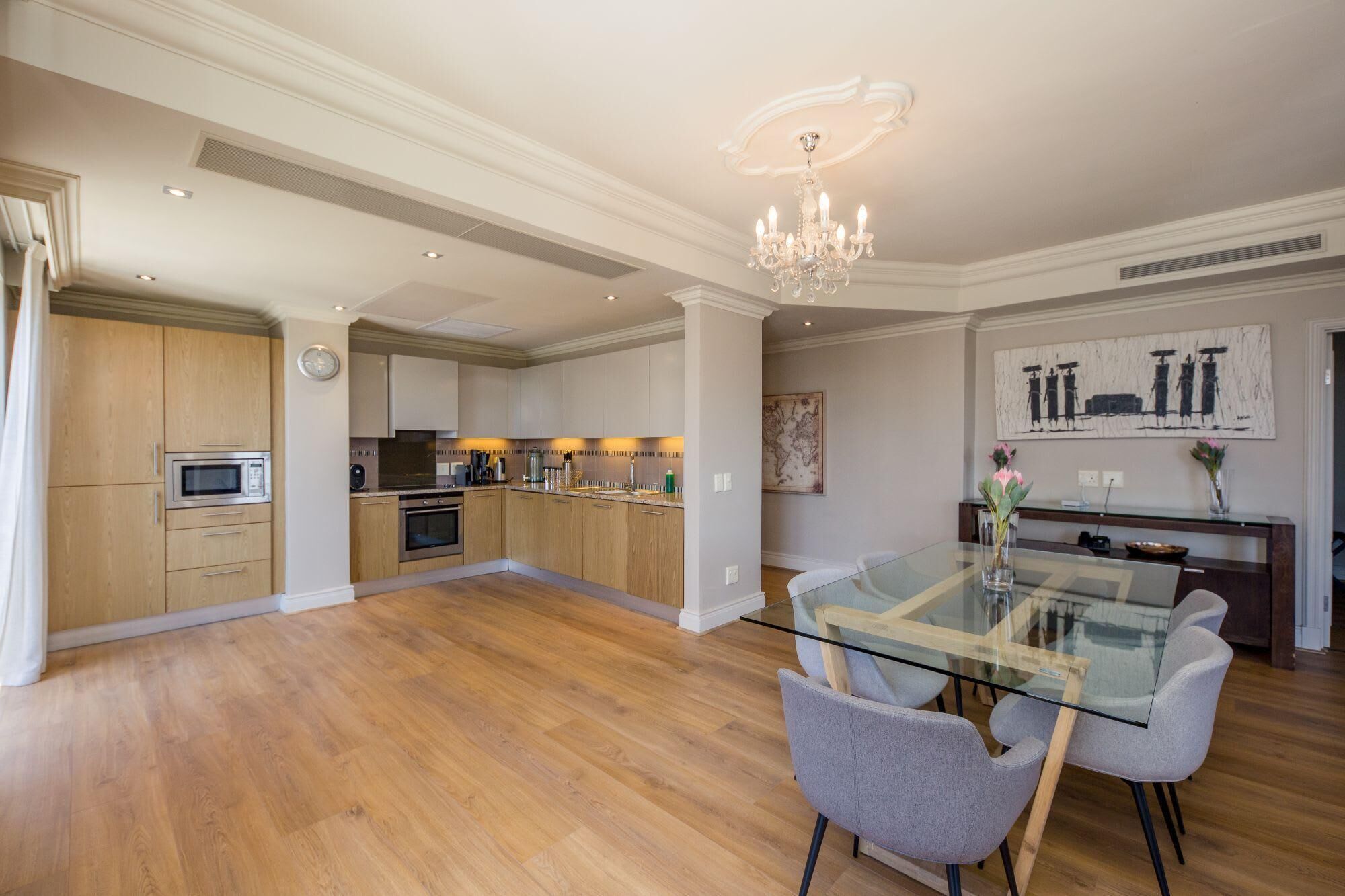 A spacious kitchen with wooden cabinets, a glass dining table, and a chandelier.