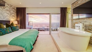A modern hotel room with a large bed, a bathtub, and a balcony with a city view. - Stylish Holiday Apartment w Private Pool 180 Views Malibu (Cape Town)