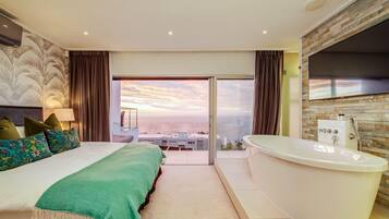 A modern hotel room with a large bed, a bathtub, and a balcony with a city view.