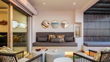 A modern living room with a grey sofa, round white side tables, and black wicker chairs.