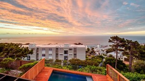 A residential area with a swimming pool, modern buildings, and a view of the sea during sunset. - Stylish Holiday Apartment w Private Pool 180 Views Malibu (Cape Town)