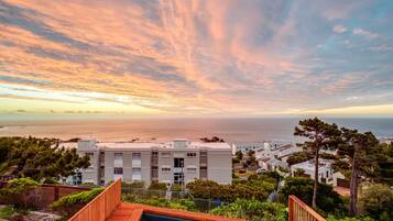 A residential area with a swimming pool, modern buildings, and a view of the sea during sunset.