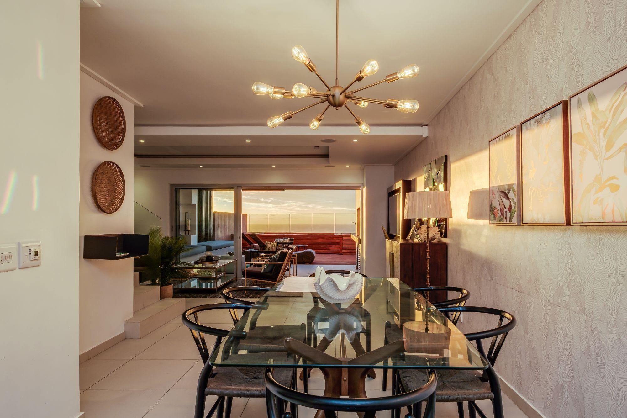 A modern dining area with a glass table and chairs, a unique chandelier, and artwork on the walls.