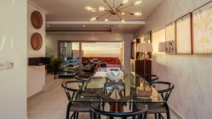 A modern dining area with a glass table and chairs, a unique chandelier, and artwork on the walls. - Stylish Holiday Apartment w Private Pool 180 Views Malibu (Cape Town)