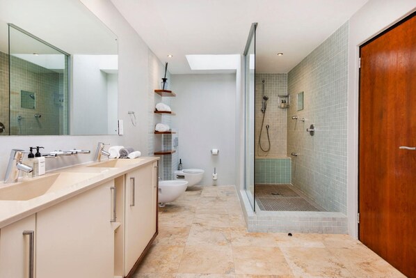 A modern bathroom with a large mirror, a beige vanity, a white toilet, and a glass-enclosed shower area.
