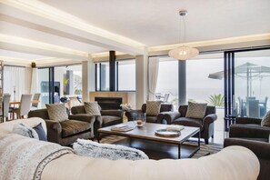Un salon spacieux doté d’une cheminée, de sièges confortables et de grandes fenêtres offrant une vue sur l’extérieur.