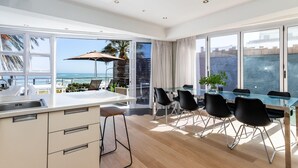 A modern kitchen with a large island, dining area with chairs, and a view of the ocean. - Beautiful 3bedroom Seaside Apartment Paloma Apartment (Cape Town)