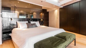 A modern bedroom with a large bed, a green bench, a marble headboard, and a dark wardrobe. - Beautiful 3bedroom Seaside Apartment Paloma Apartment (Cape Town)