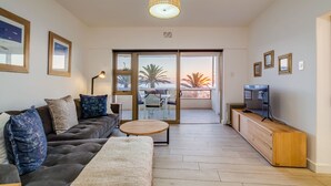 A modern living room with a sofa, coffee table, TV, and a balcony with a view. - Beautiful Lock up go w Ocean Views Sundowner Views (Cape Town)