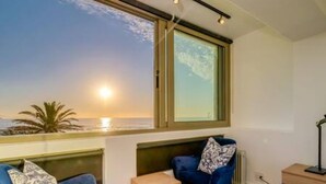 A room with a large window overlooking the sea, a blue chair, a small table, and a radiator. - Beautiful Lock up go w Ocean Views Sundowner Views (Cape Town)