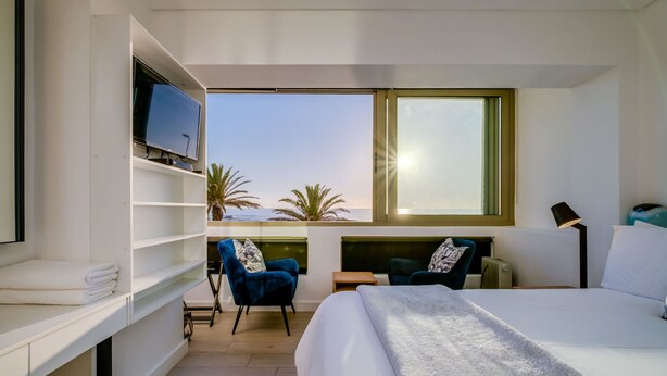 A modern hotel room with a large bed, a TV on a shelf, a desk, two chairs, and a view of the ocean. - Beautiful Lock up go w Ocean Views Sundowner Views (Cape Town)