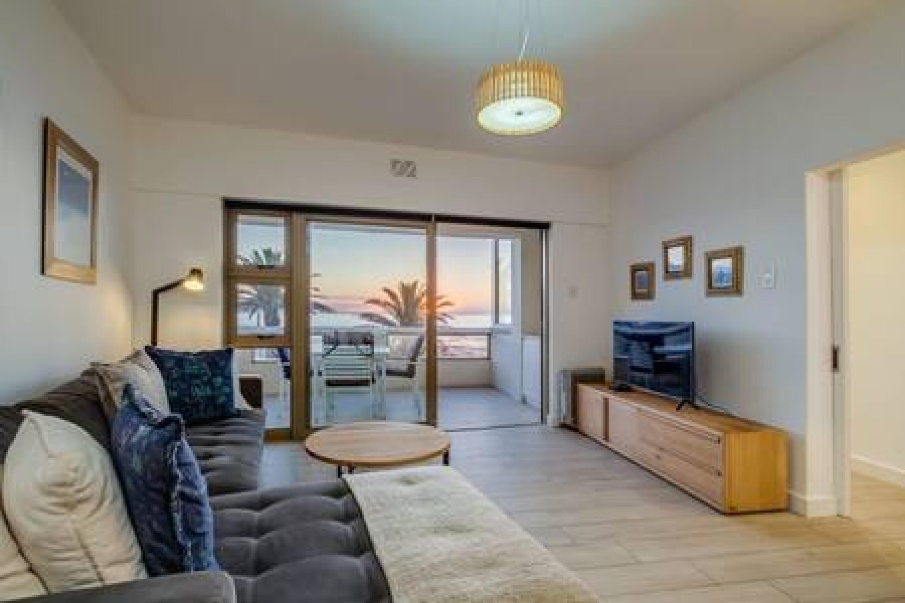 Un soggiorno moderno con divano, tavolino, televisore su mobile in legno e balcone con vista.