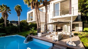A modern two-story house with a pool, outdoor furniture, and palm trees. - Unique Villa w Pool Garden and Sea Views Lobster Villa (Cape Town)