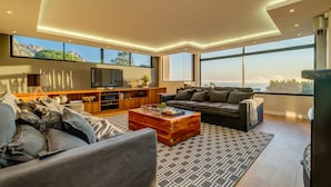 Un salon moderne doté d’un grand téléviseur, de sièges confortables et offrant une vue sur l’extérieur.