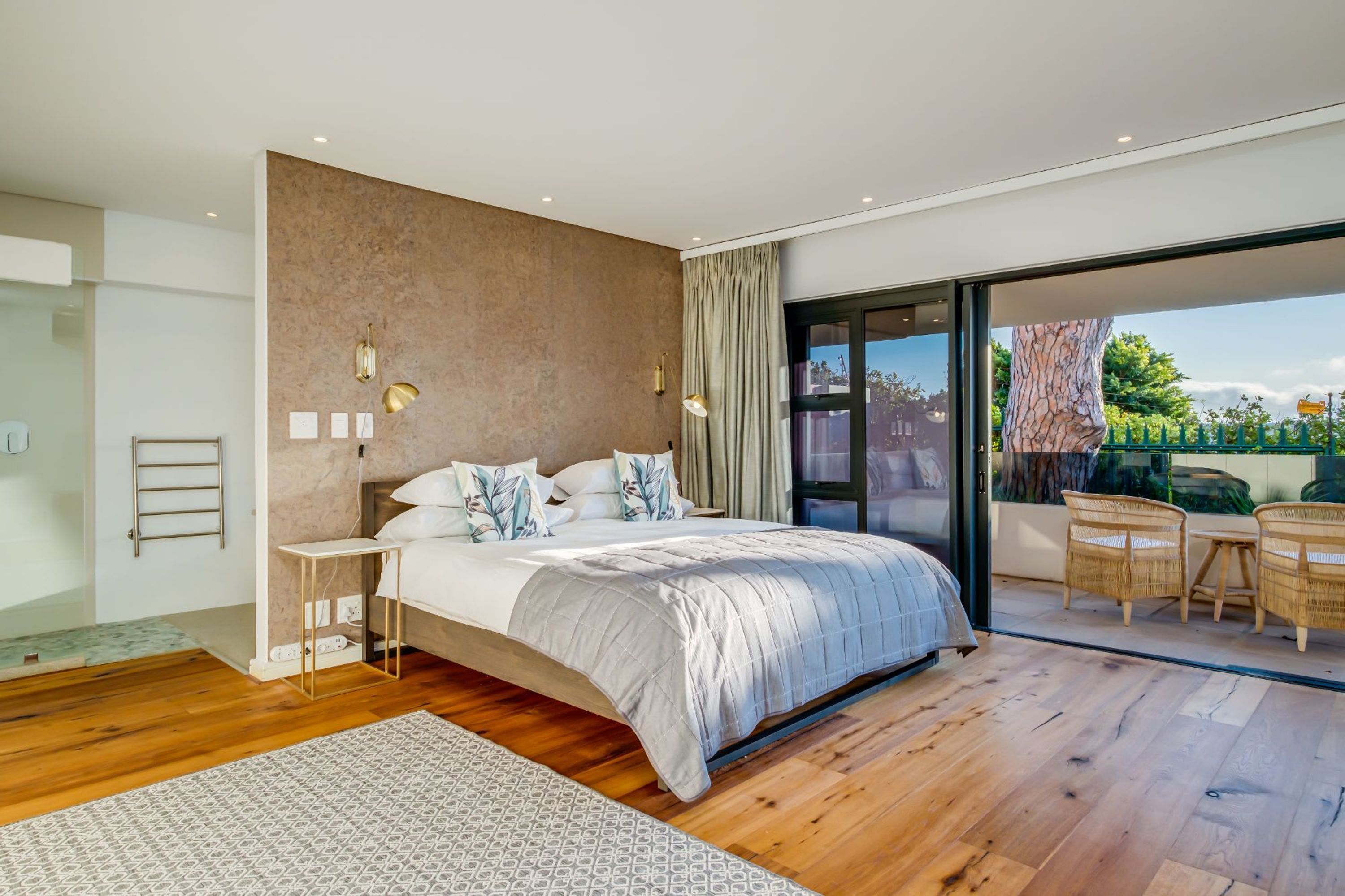Un dormitorio moderno con una cama grande, una mesita de noche pequeña, una lámpara de pared y vistas al exterior.