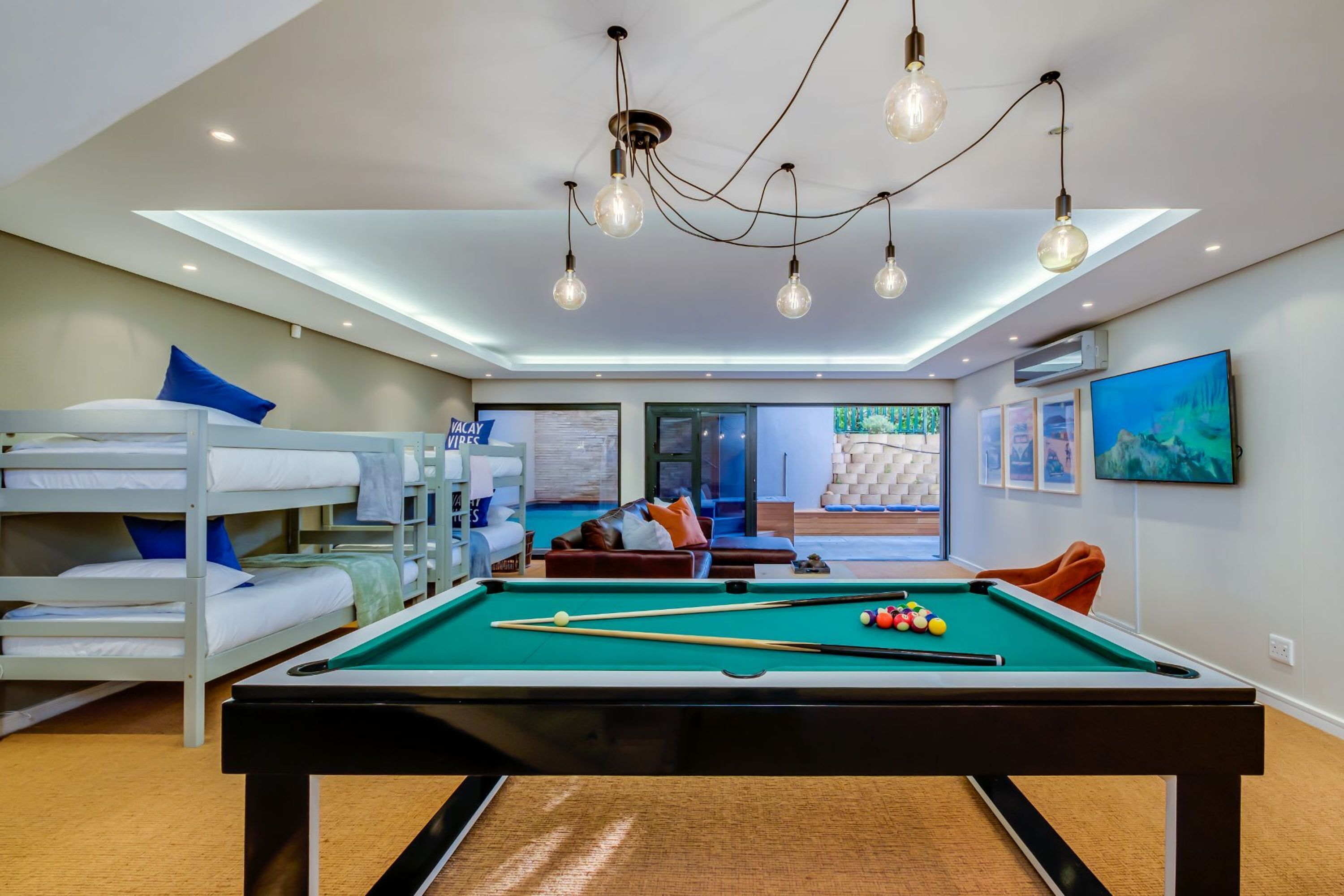 Une table de billard avec des billes, un lit superposé avec des oreillers, un canapé, un téléviseur et un luminaire au plafond.