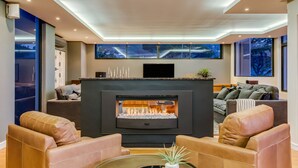Un salon moderne doté d’une cheminée, de canapés en cuir, d’un téléviseur à écran plat et de grandes fenêtres.