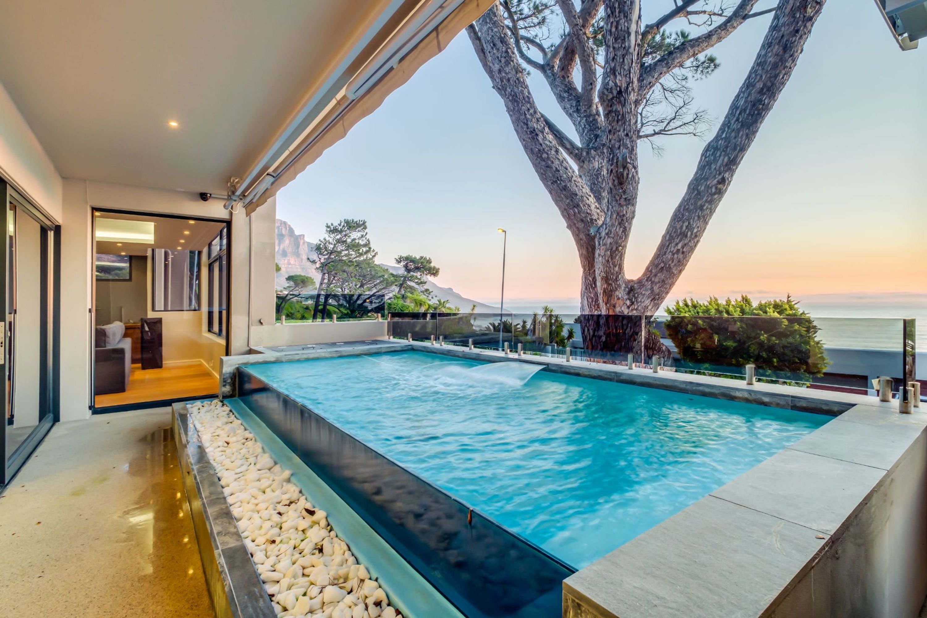 A modern pool with a clear view of the surrounding landscape, including a large tree and distant mountains.