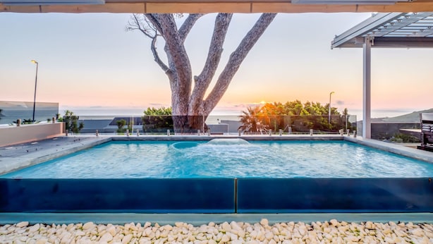 Une piscine avec un grand arbre en arrière-plan, entourée d’une zone abritée d’où l’on peut admirer l’océan.